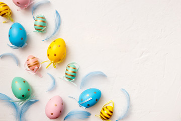 Easter colored eggs with feathers on white background. Happy Easter greeting card minimal concept. Top view, flat lay, copy space.