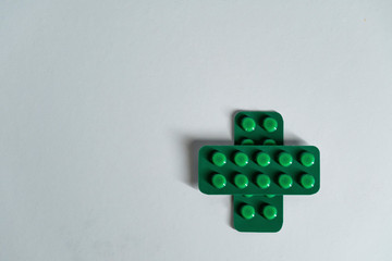Medical cross sign made of two green blisters with pills isolated on grey background. Healthcare concept.