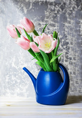 A beautiful bouquet of pink tulips in a water can on a light background.
