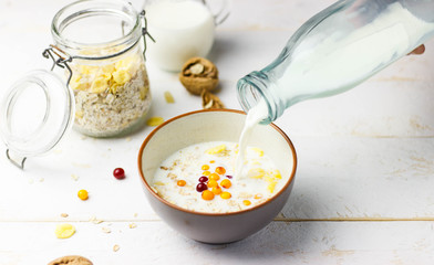 Milk is poured from a bottle into a bowl with granola and berries. 