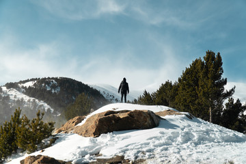 Naklejka na ściany i meble a young man dressed in black on top of a rock with the background of mountains among trees and snow