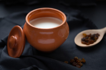 Brown pot with sour cream and a wooden spoon with raisins on a dark background.