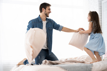 Fototapeta premium happy father and daughter playing pillow fight in bed at morning