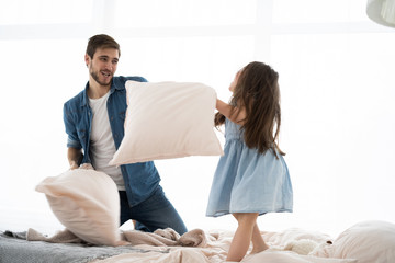 Obraz premium happy father and daughter playing pillow fight in bed at morning