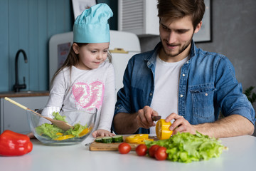 Handsome man and his little cute daughter are cooking on kitchen. Making salad. Healthy lifestyle concept.