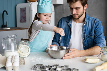 Daddy with daughter baking cake together in home kitchen.