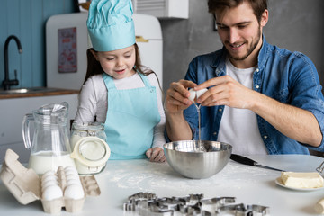 Daddy with daughter baking cake together in home kitchen.