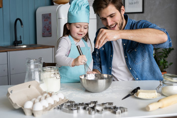 Daddy with daughter baking cake together in home kitchen.