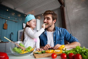 Handsome man and his little cute daughter are cooking on kitchen. Making salad. Healthy lifestyle concept.