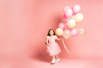 Happy celebration of birthday party with flying balloons of charming cute little girl in tulle dress smiling to camera isolated on pink background. Charming smile, expressing happiness