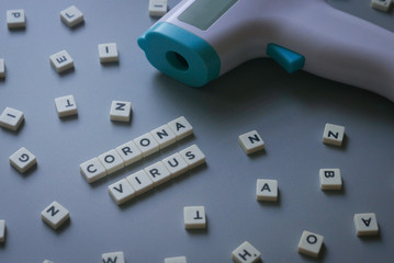 Cube alphabet written with Corona Virus with non contact thermometer on grey background.