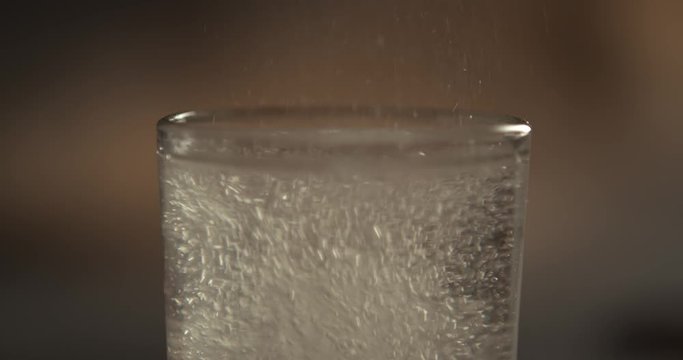 Effervescent aspirin tablet dropping to glass of water, close up slow motion fizzy pill falls and dissolves with bubbles. Medicine, health care pharmacy chemistry concept