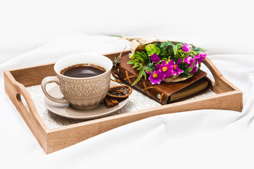 Fresh morning coffee with wrapped flowers on a board on a bed sheet 