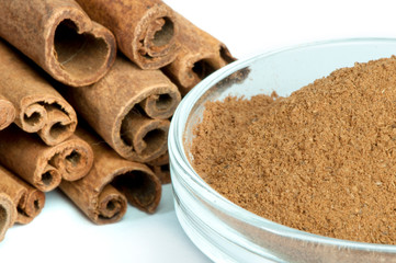 Powdered cinnamon in bowl and cinnamon sticks