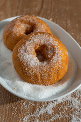 Close-up of two donuts in plate with sugar on wooden board and sugar in vertical with copy space