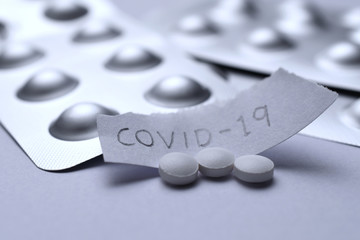 White pill tablet with paper text COVID-19. Corona virus flu dose of medicine or treatment drug...