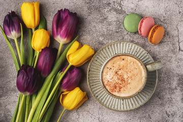 purple and yellow tulips, cup with coffee and macaroon cookies on a gray concrete background, copy space