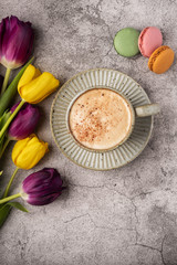 purple and yellow tulips, cup with coffee and macaroon cookies on a gray concrete background, copy space