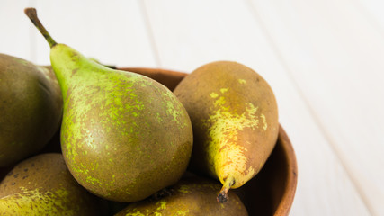 still life, green pears in a wooden plate on a white table, close-up