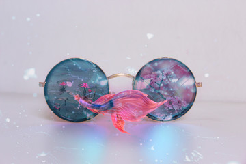Photocomposition of sunglasses and pink florals scenery and. swimming fish