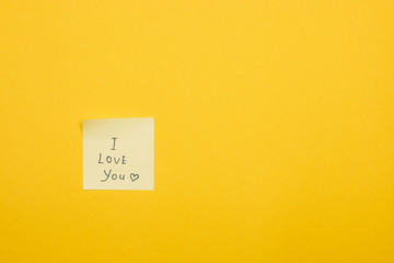 i love you and a heart hand writing on yellow sticky note against yellow background with copy space