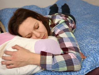 Tired and exhausted woman hugging a pillow lying down on her stomach in bed and napping or sleeping