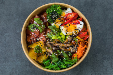 Poke bowl with salmon, guinoa, vegetables, friut and tofu on dark background