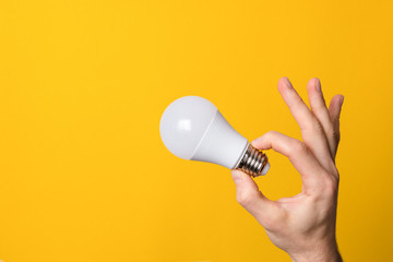 ok gesture closeup hand holding white led lighting bulb against a yellow wide background banner with copyspace. concept of idea, energy and ecology