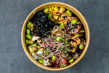 Poke bowl with salmon, guinoa, vegetables, friut and tofu on dark background