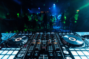 professional music DJ mixer in a booth in a nightclub on the background of blurred silhouettes of...