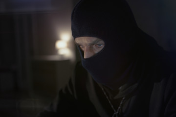 Male hacker in the hood in a dark room using computer virus program for cyber attack. Hackers and cyber security concept                               