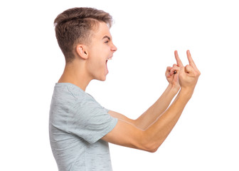 Angry teen boy showing middle finger - side view, isolated on white background. Portrait of caucasian young teenager showing bad gesture and screaming. Upset cute child doing obscene sign - profile. - 329541197