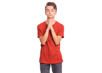 Portrait of teen boy praying, isolated on white background. Cute caucasian teenager with hands folded in prayer hoping for better. Child asking God for good luck, success or forgiveness.