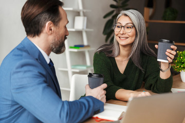 Photo of colleagues talking and drinking coffee while working on laptop