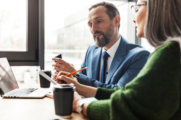 Photo of colleagues talking while working with laptop and documents