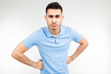 Caucasian serious man in a blue T-shirt put his hands on his hips on a white studio background