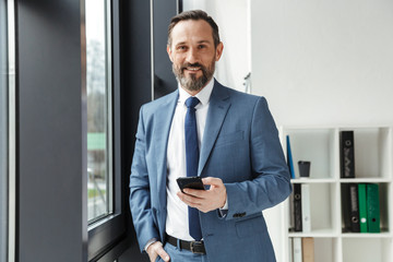 Photo of bearded smiling businessman in formal suit typing on cellphone