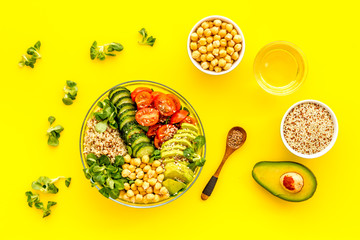 healhty vegan lunch bowl. Avocado, quinoa, sweet potato, tomato, spinach and chickpeas vegetables salad om yellow table. Top view