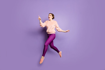 Full length photo of funny lady jumping up high see low shopping prices direct finger advert banner walking down street wear casual stylish pullover pants isolated purple color background