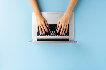 Fototapeta na wymiar Overhead shot of woman’s hands using laptop on blue table. Office desktop. Flat lay