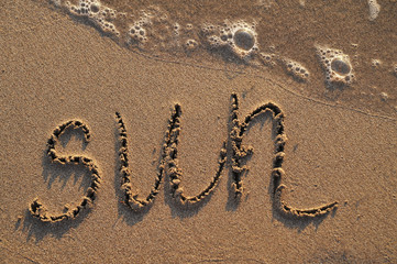Sun written on sand background.