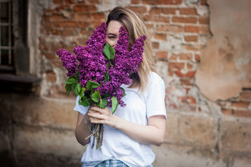 Woman holding a vivid bunch of lilac flowers against brick wall