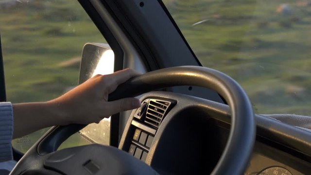 Man hand on car wheel driving on a landscape road at golden hour