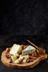 Cheese platter with honey and various nuts on an authentic wooden board. Dark black embossed background. Appetizer, aperitif, snack table