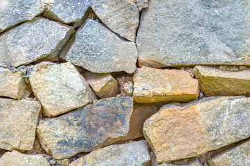 A wall made of large rough brown, gray and beige natural stones.Сoncept of background, decoration, wallpaper.Selective focus.