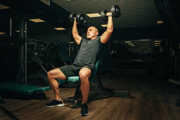 Fototapeta na wymiar Bodybuilder doing exercises with dumbbells in a dark gym