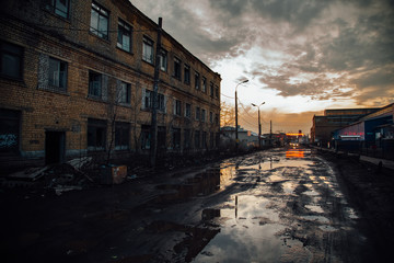 Old industrial area in evening. Dirty pools on cracked asphalt of damaged road