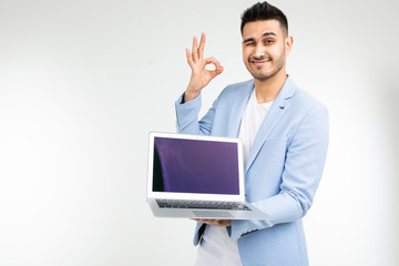 smiling young brunette man joyfully holds a laptop with blank for inserting a website page on a white background with copy space