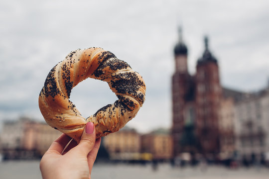 Tourists holding bagel obwarzanek traditional polish cuisine snack on Market square in Krakow. Travel Europe