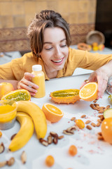 Portrait of a young and joyful woman holding bottle of juice at the table full of healthy raw vegetables and fruits. Concept of vegetarianism, detox, healthy eating and wellness